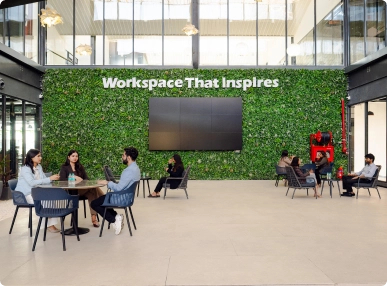 Three professionals talking at a round table in a modern DevX Gift City office with 'Workspace That Inspires' sign.