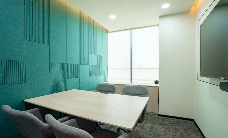 Small modern meeting room with a wooden table, four gray chairs, teal paneled wall, and a wall-mounted screen at Walter P Moore.