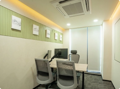 Small office with three chairs, a desk, dual monitors, and framed pictures on a green and beige wall at Walter P Moore.