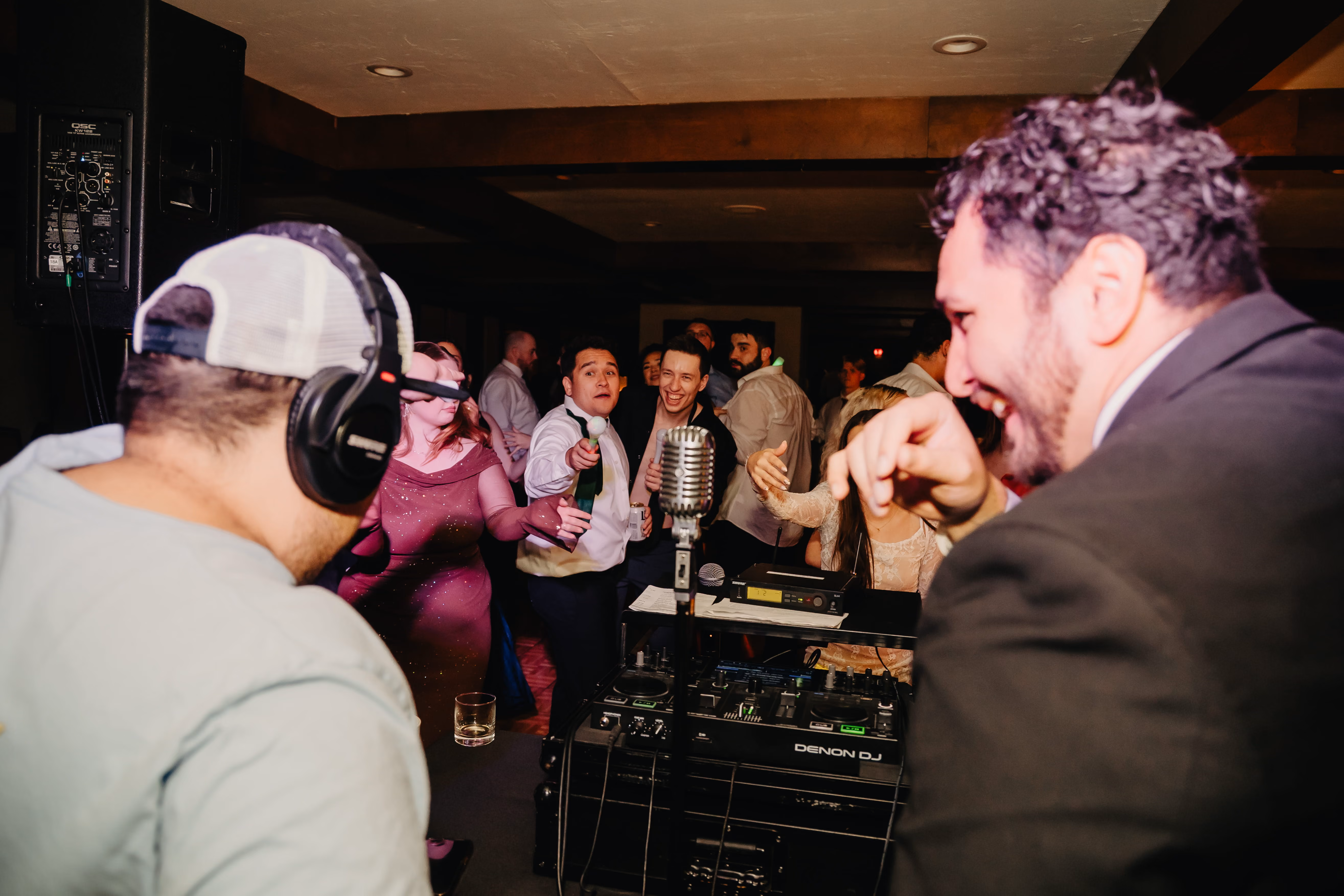 Point of view behind a DJ booth with a DJ and guest creating music for the crowd.