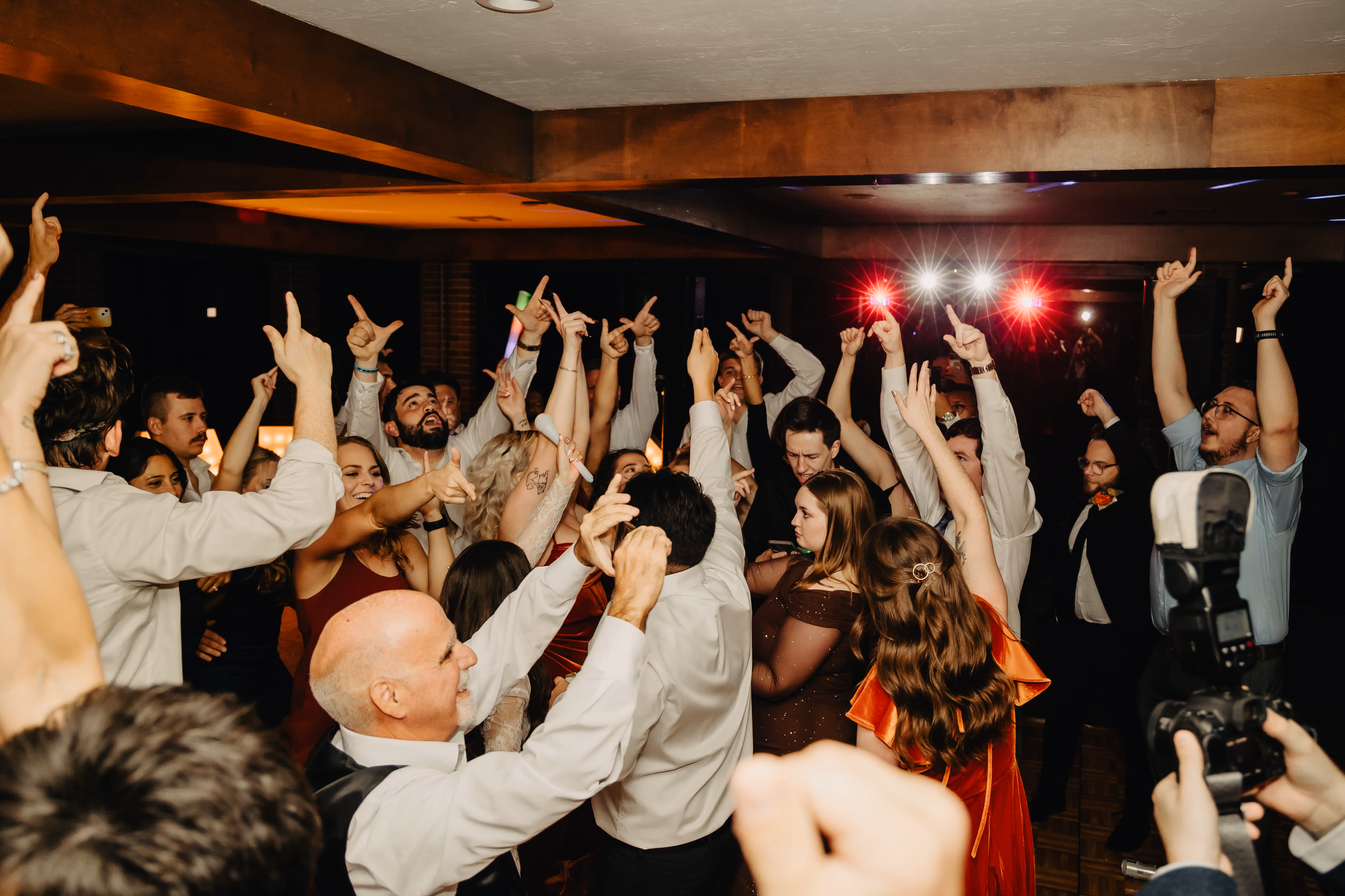 A dance floor full of wedding guests dancing with their hands in the air.