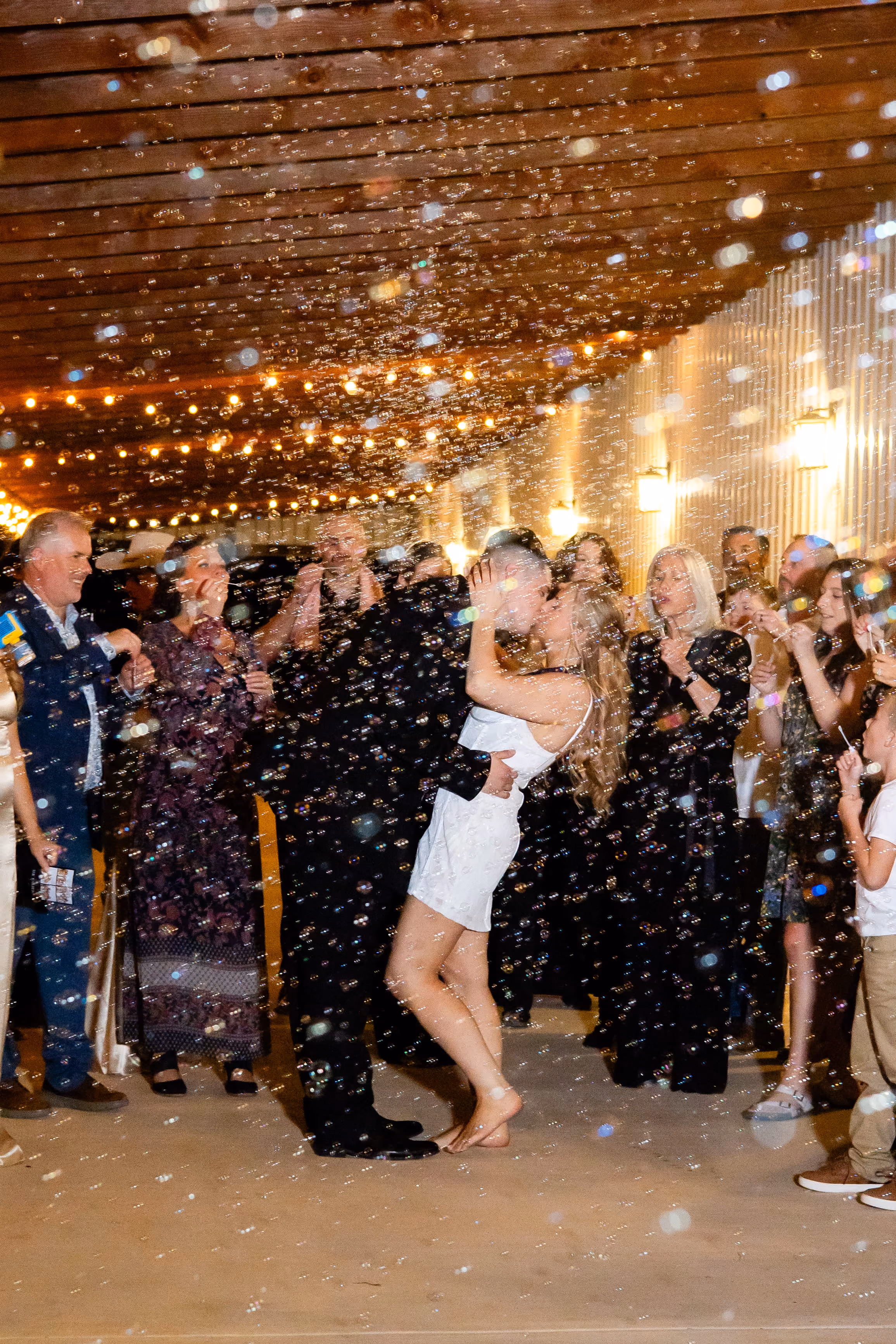 A bride and groom are kissing being surrounded by bubbles at their grand exit
