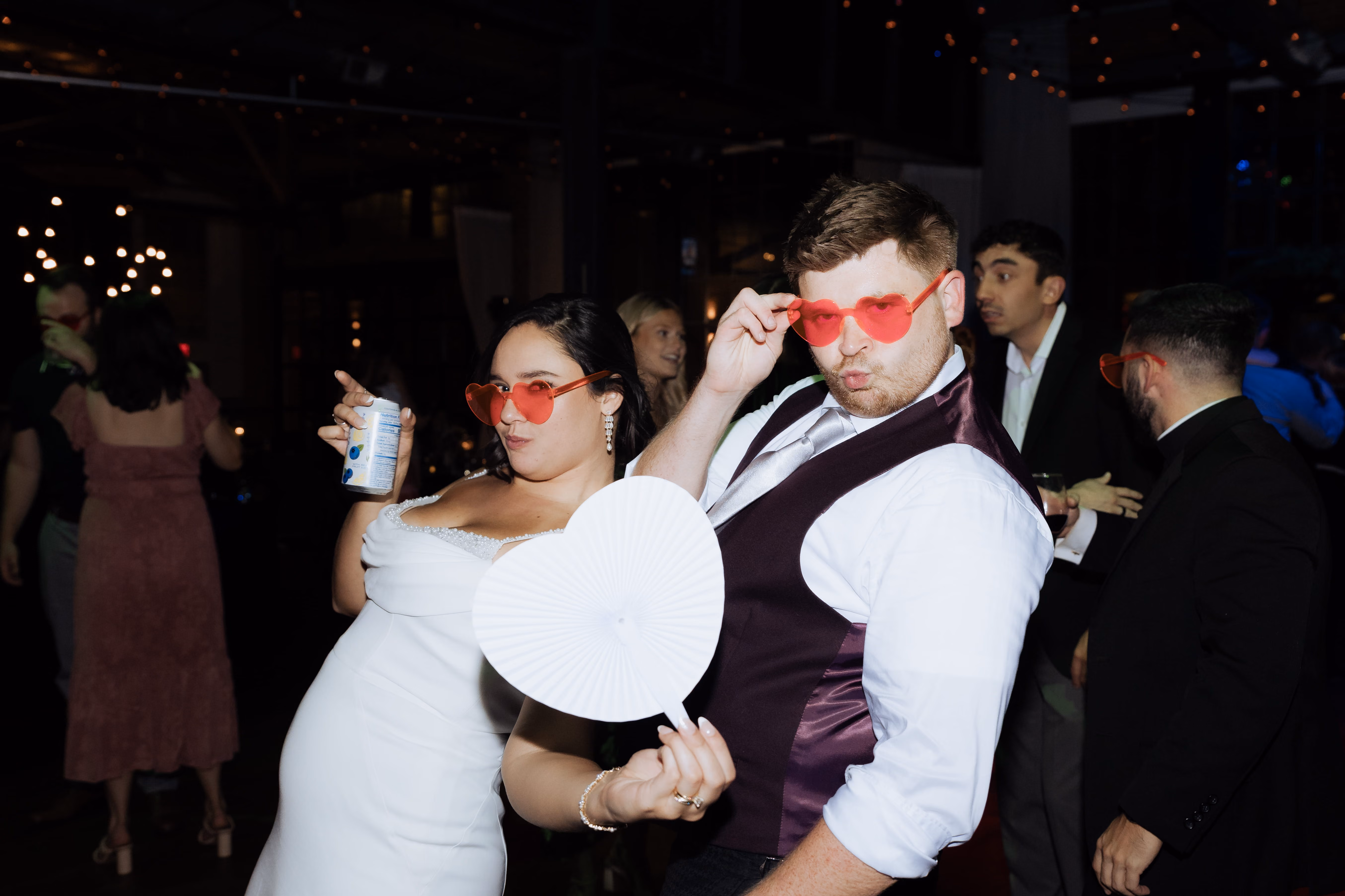 During a wedding reception, the bride and groom pose wearing pink heart glasses.