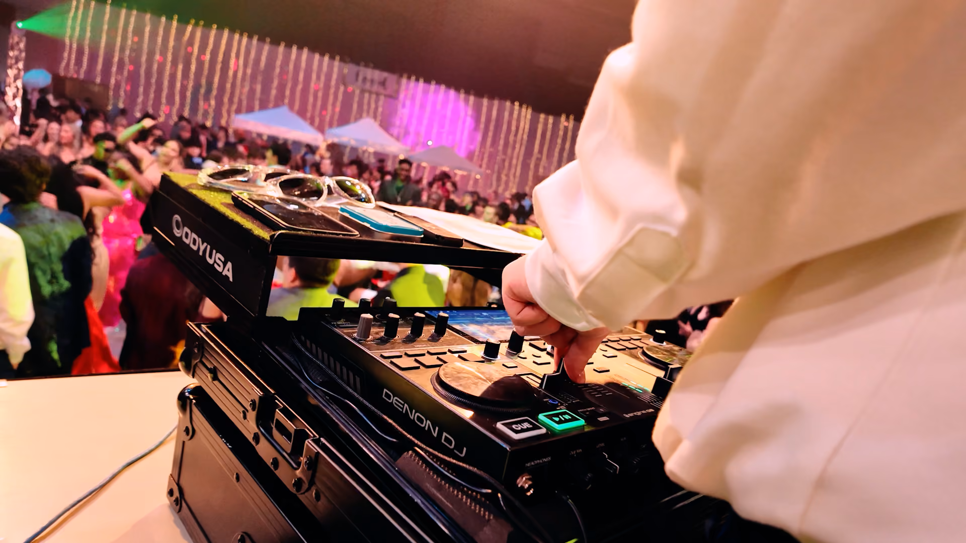 A point of view from a behind a DJ booth with students dancing in the background.