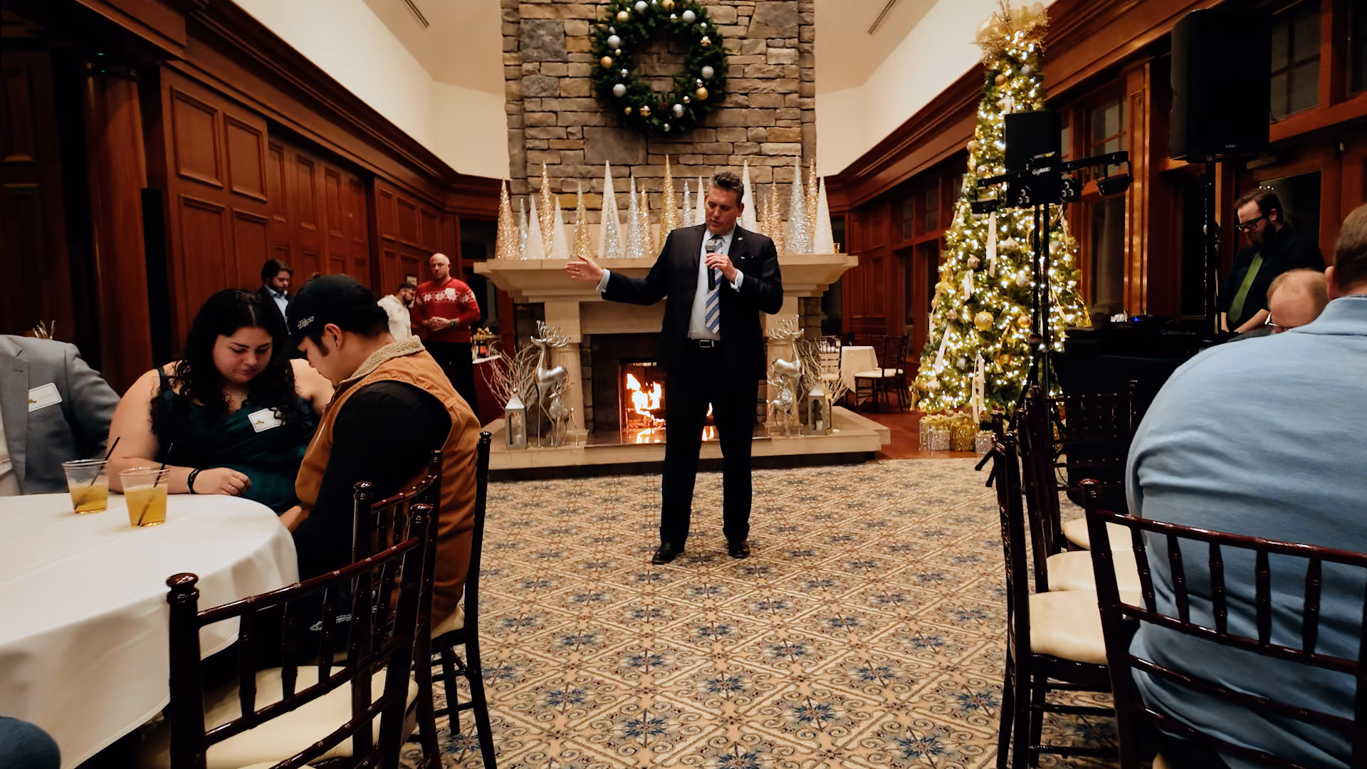 A corporate holiday party with a MC standing in the middle of the room giving an announcement.