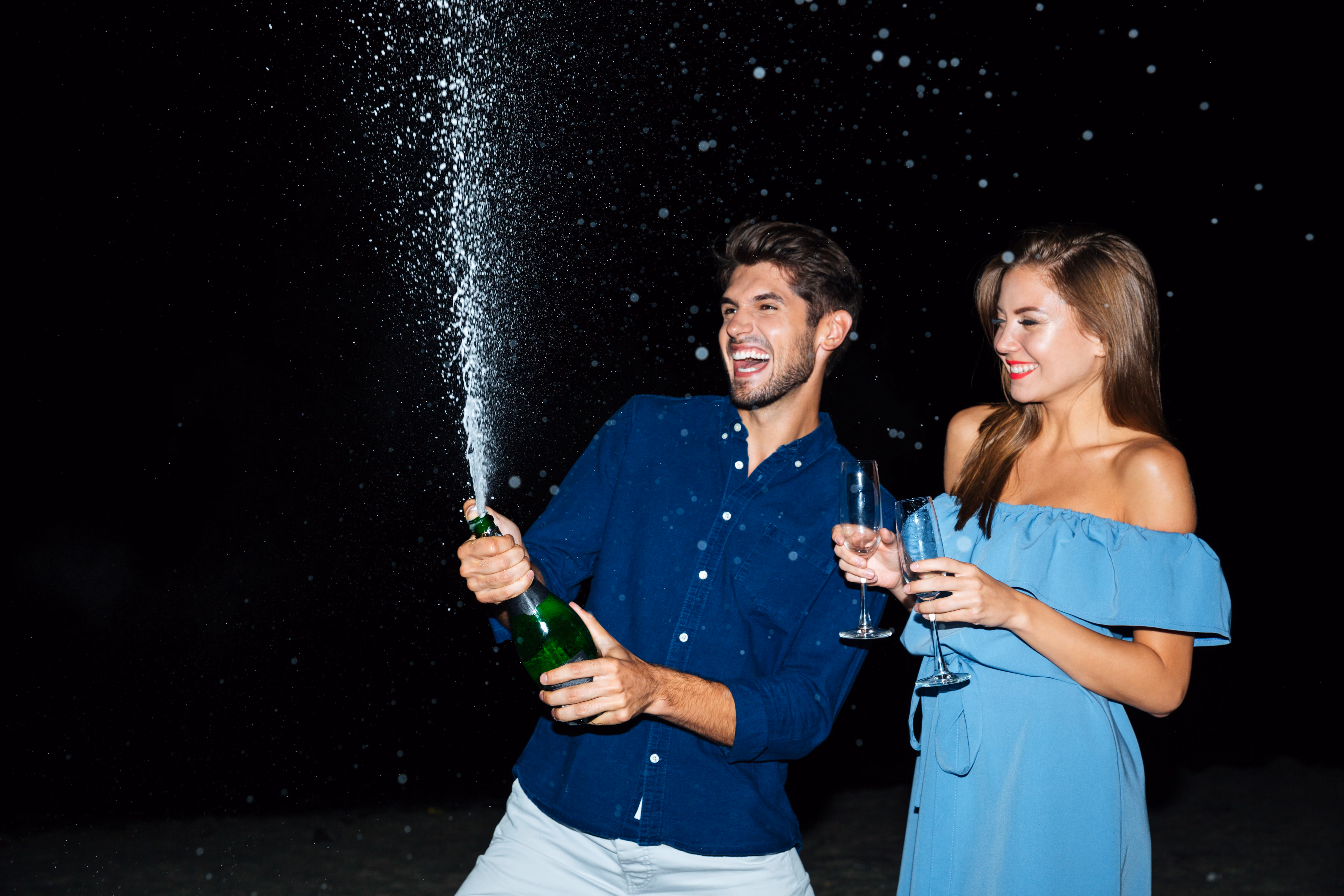 A women and man couple celebrating with a bottle of champagne spraying outwards.
