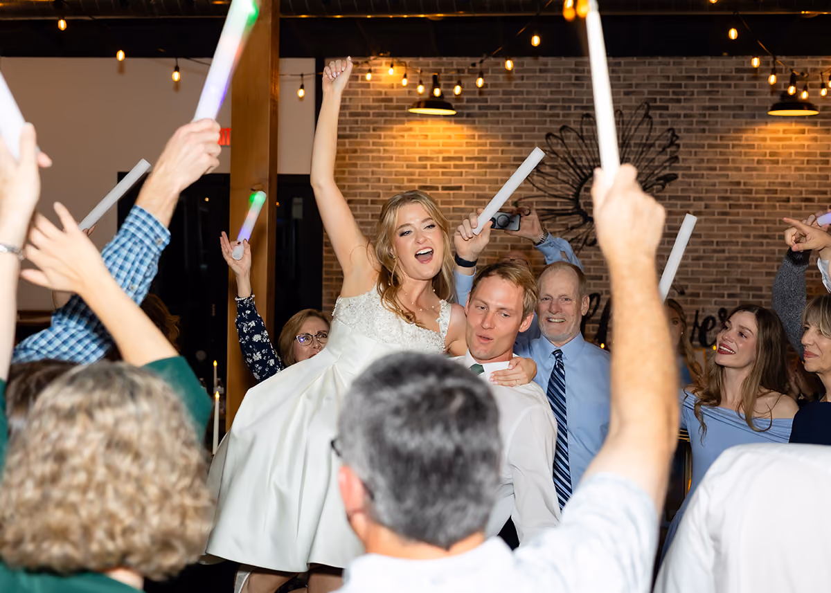 A groom holding his bride while the guests dance in a circle raising LED glow tubes.