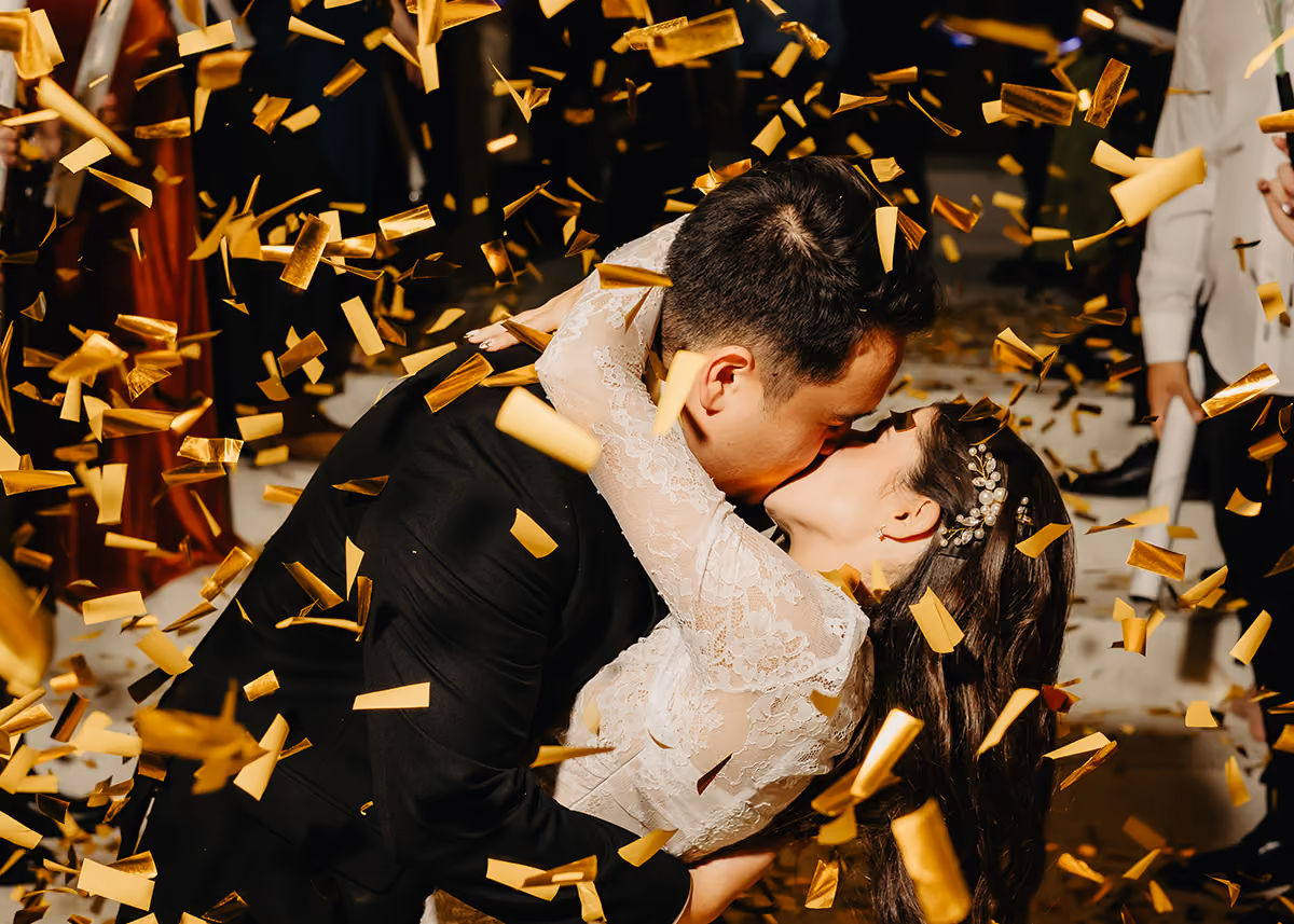 A newly married couple kissing with gold confetti flying around them. 
