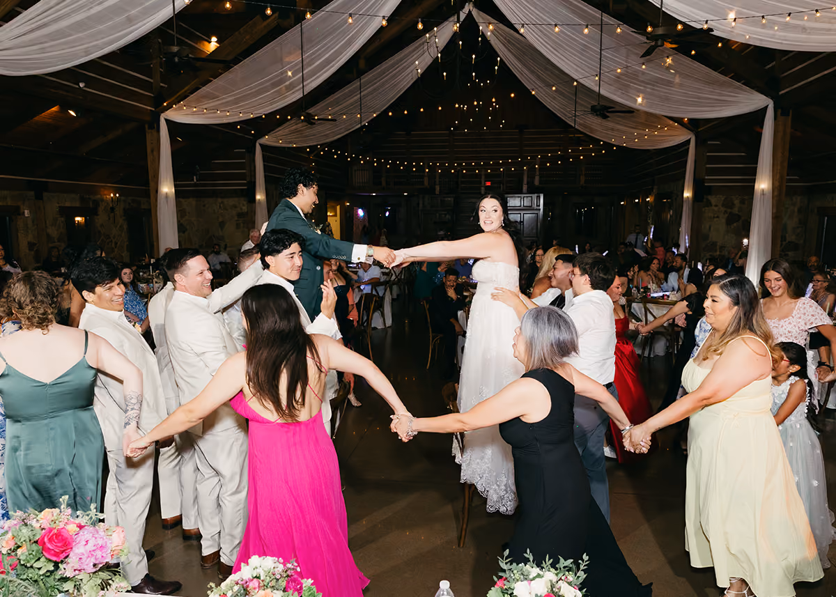 A wedding reception with the bride and groom standing on chairs while the guests dance around them.