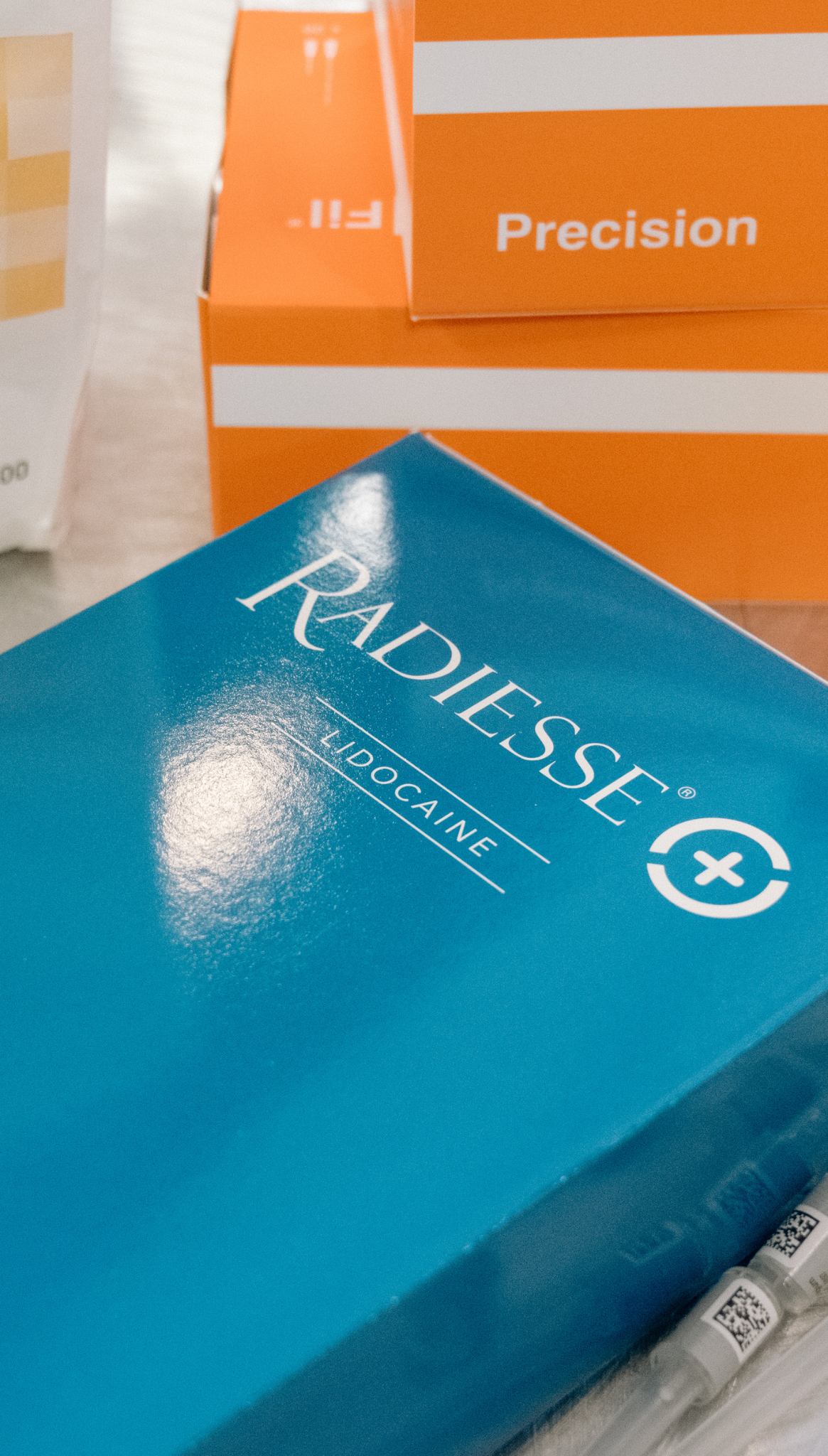 Blue Radiesse Lidocaine box with orange Precision boxes stacked behind and syringes below.
