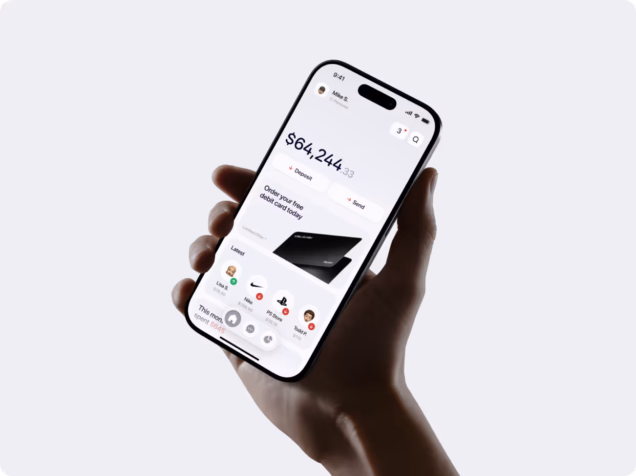 Hand holding a smartphone displaying a financial app with a $64,244.33 balance and options to deposit, send money, and order a free debit card.