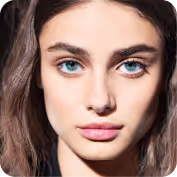 Close-up portrait of a young woman with straight brown hair and blue-green eyes looking directly at the camera.