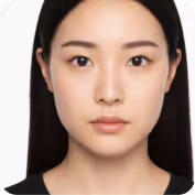 Close-up portrait of a young woman with straight black hair and neutral expression against a white background.