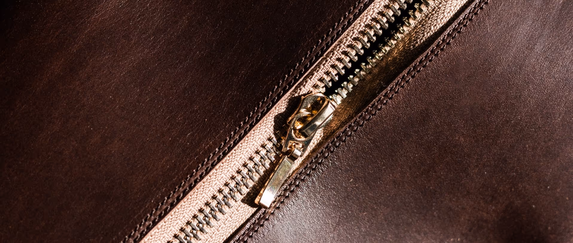 A close up of a zipper on a brown leather bag.