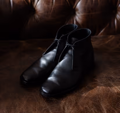 A pair of black shoes sitting on top of a brown leather couch.