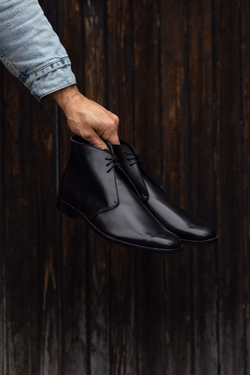 A man's hand holding a pair of black shoes.
