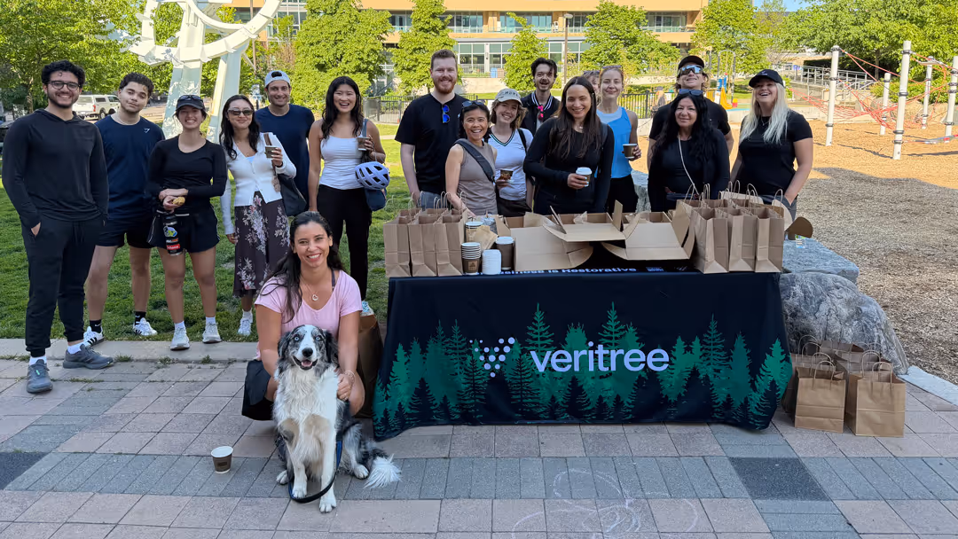 Group of people smiling behind table with Veritree logo and brown bags outdoors in a park.