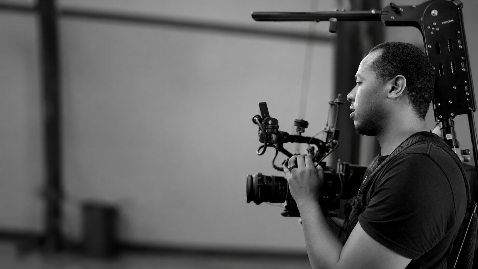 Man operating a professional video camera rig with stabilizer harness in a studio setting.