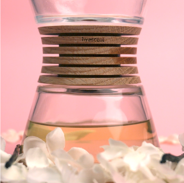 Close-up of a glass diffuser with a wooden ring labeled hyascent, surrounded by white flower petals.