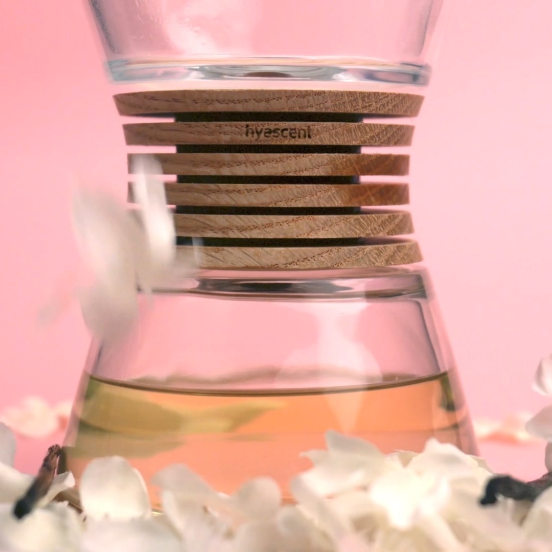 Close-up of a glass bottle with wooden slats around its neck and liquid inside, surrounded by white petals.