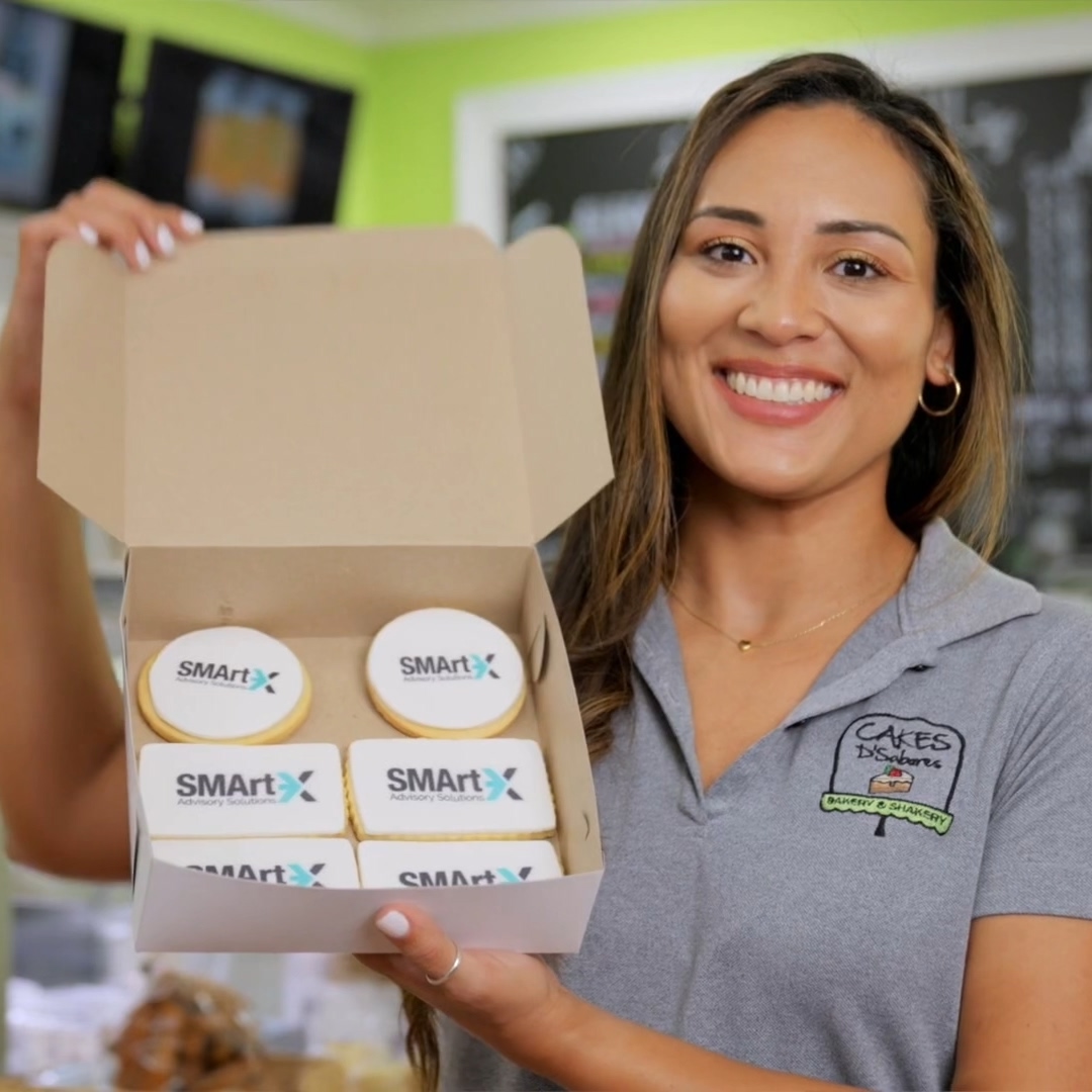 Woman smiling and holding a box with cookies decorated with SMARTX Advisory Solutions logo.
