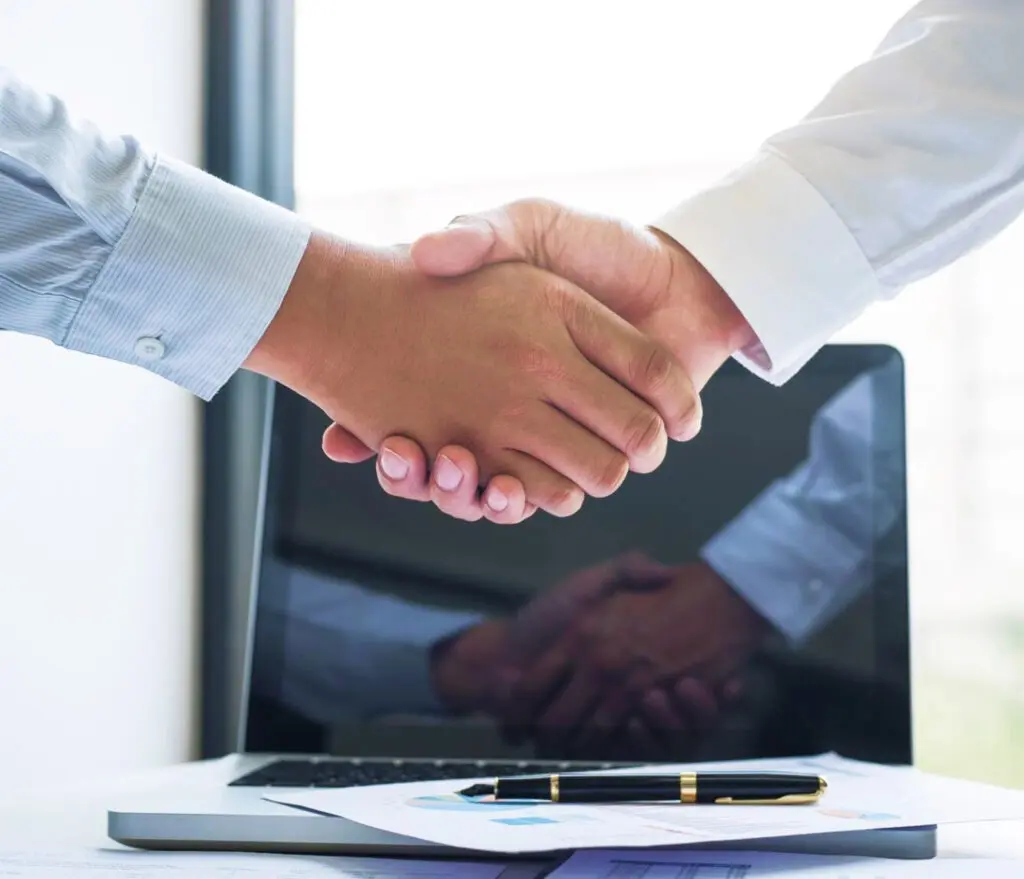 Aperto de mãos em close sobre mesa com notebook e documentos financeiros ao fundo representando a contemplação da carta de crédito no consórcio