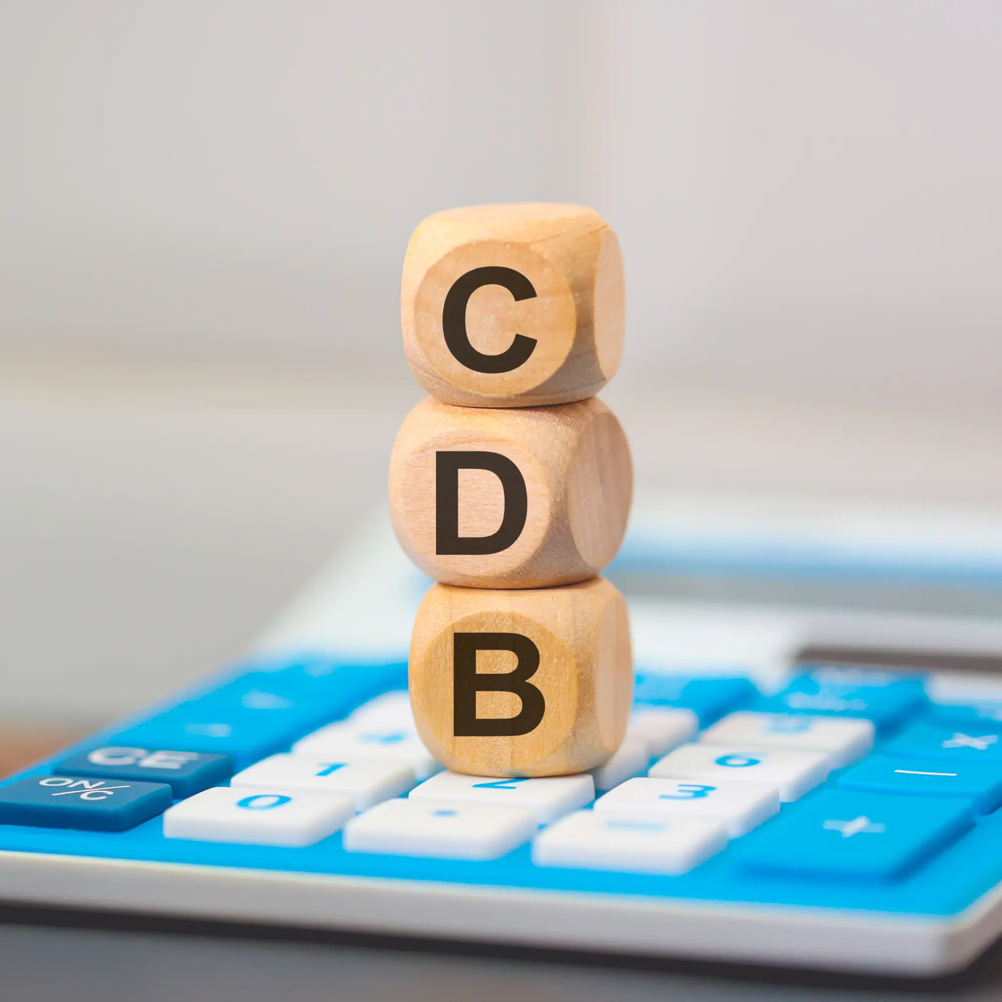 Blocos com as letras CDB sobre uma calculadora representando o cálculo do rendimento do investimento