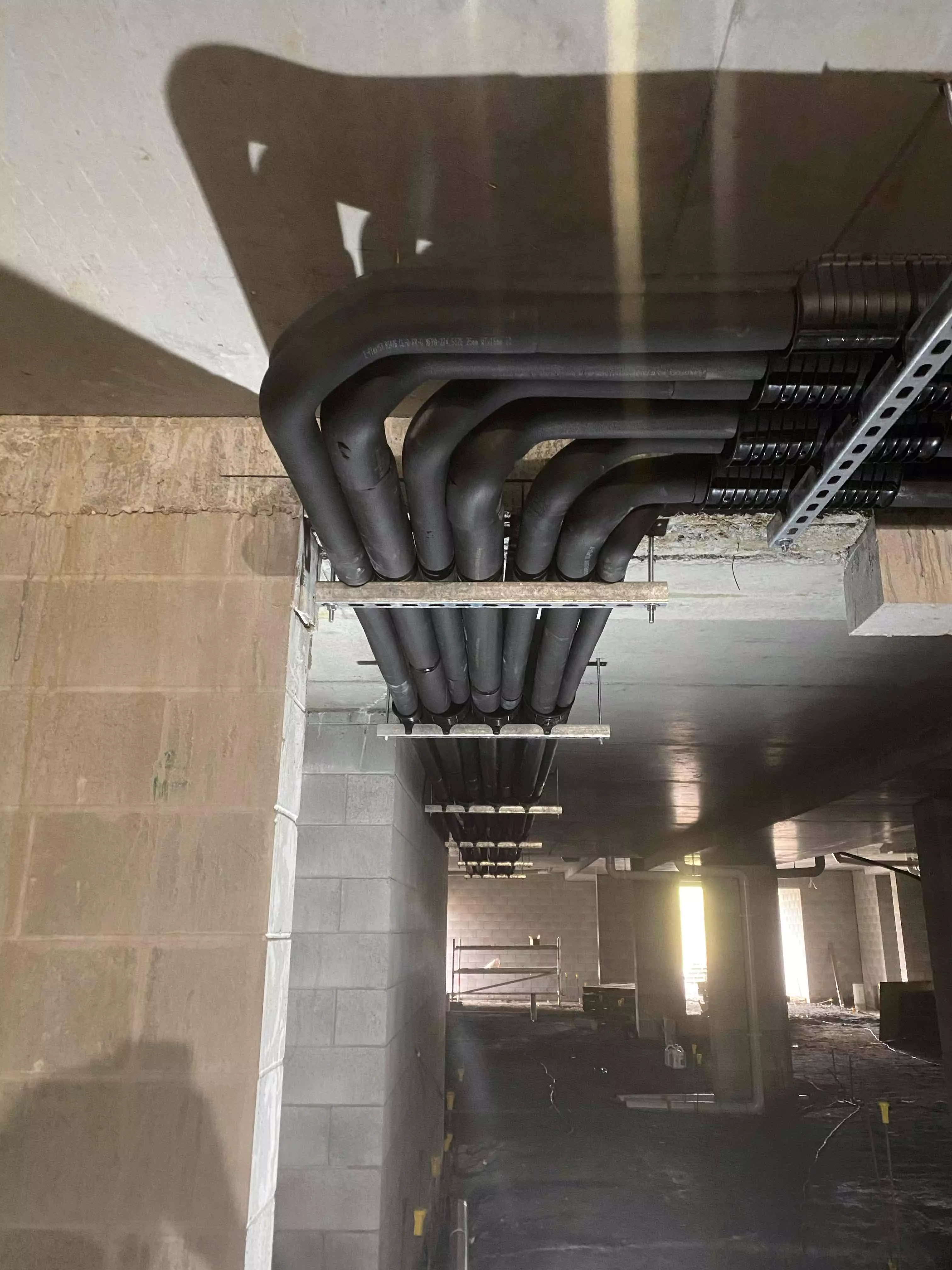 A detailed view of commercial duct installation with black insulated pipes running along the ceiling of a large building.