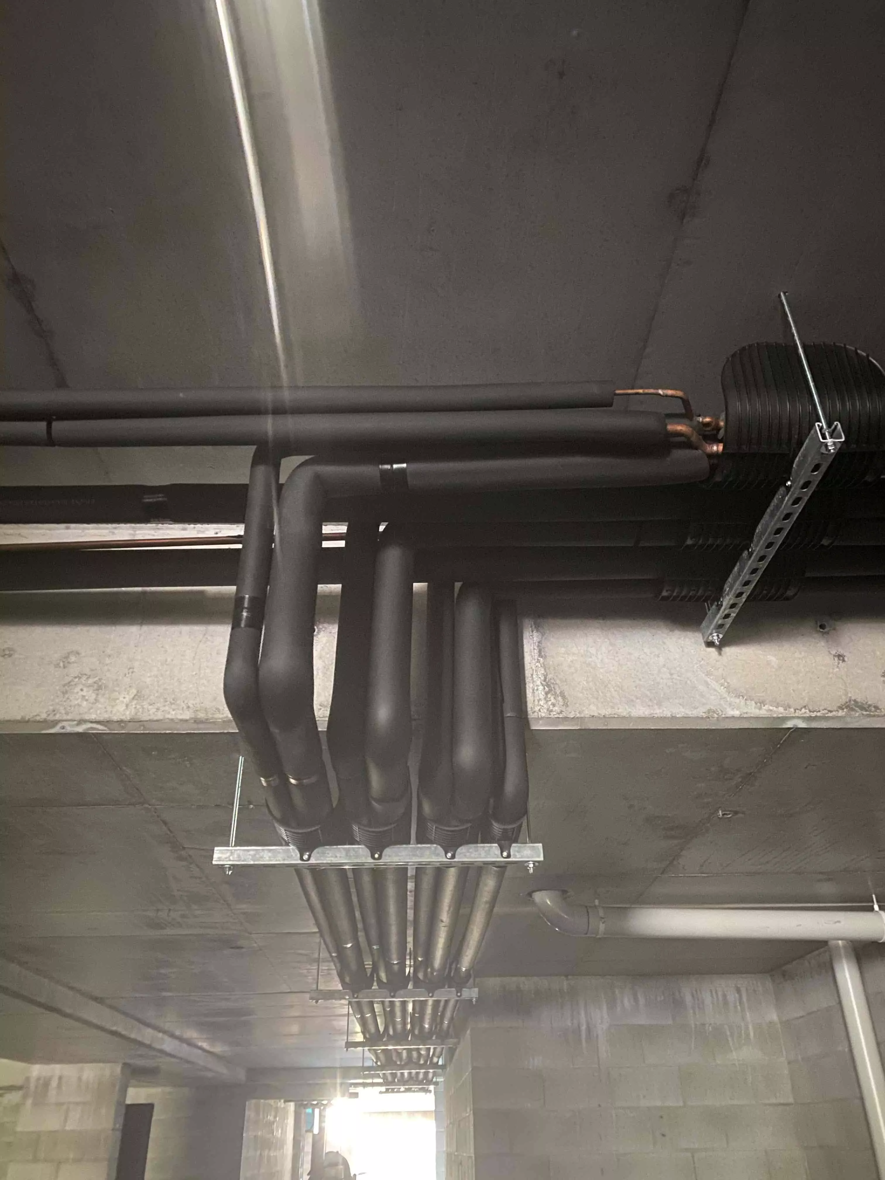 Another angle of black insulated pipes forming part of a commercial duct installation in a large building.