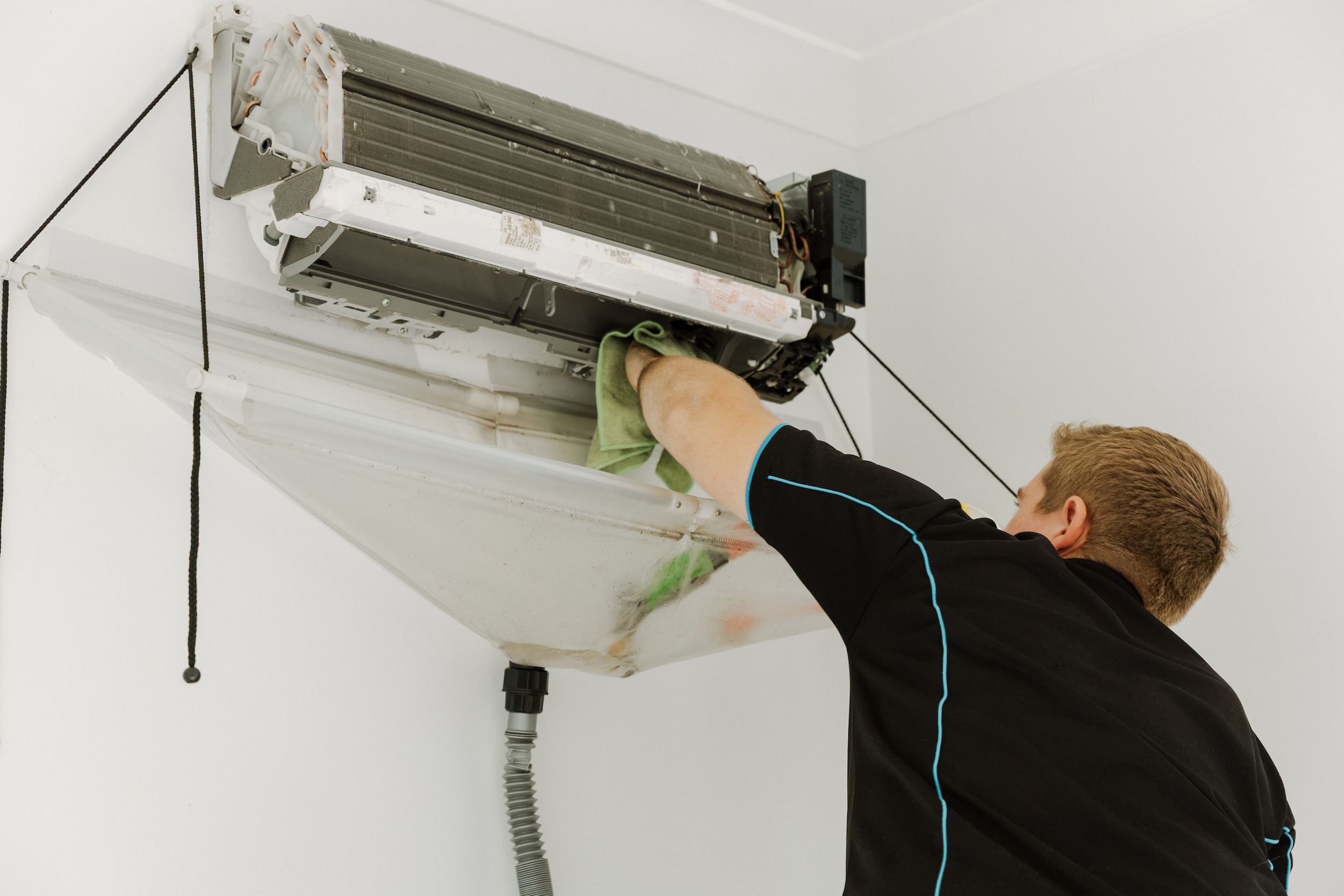 Detailed maintenance view of a technician using a cloth to meticulously clean the internal mechanics and coil of an air conditioning unit.