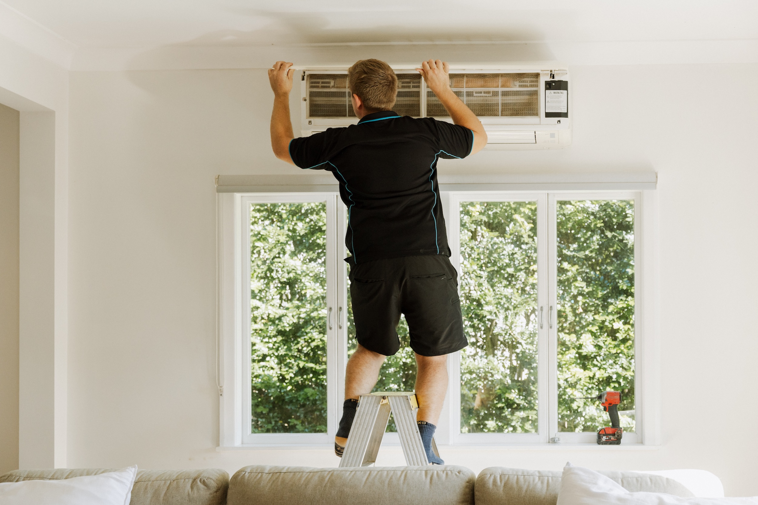 Parker Air technician standing on a step ladder to inspect and service a high-wall return air filter during a routine maintenance call.