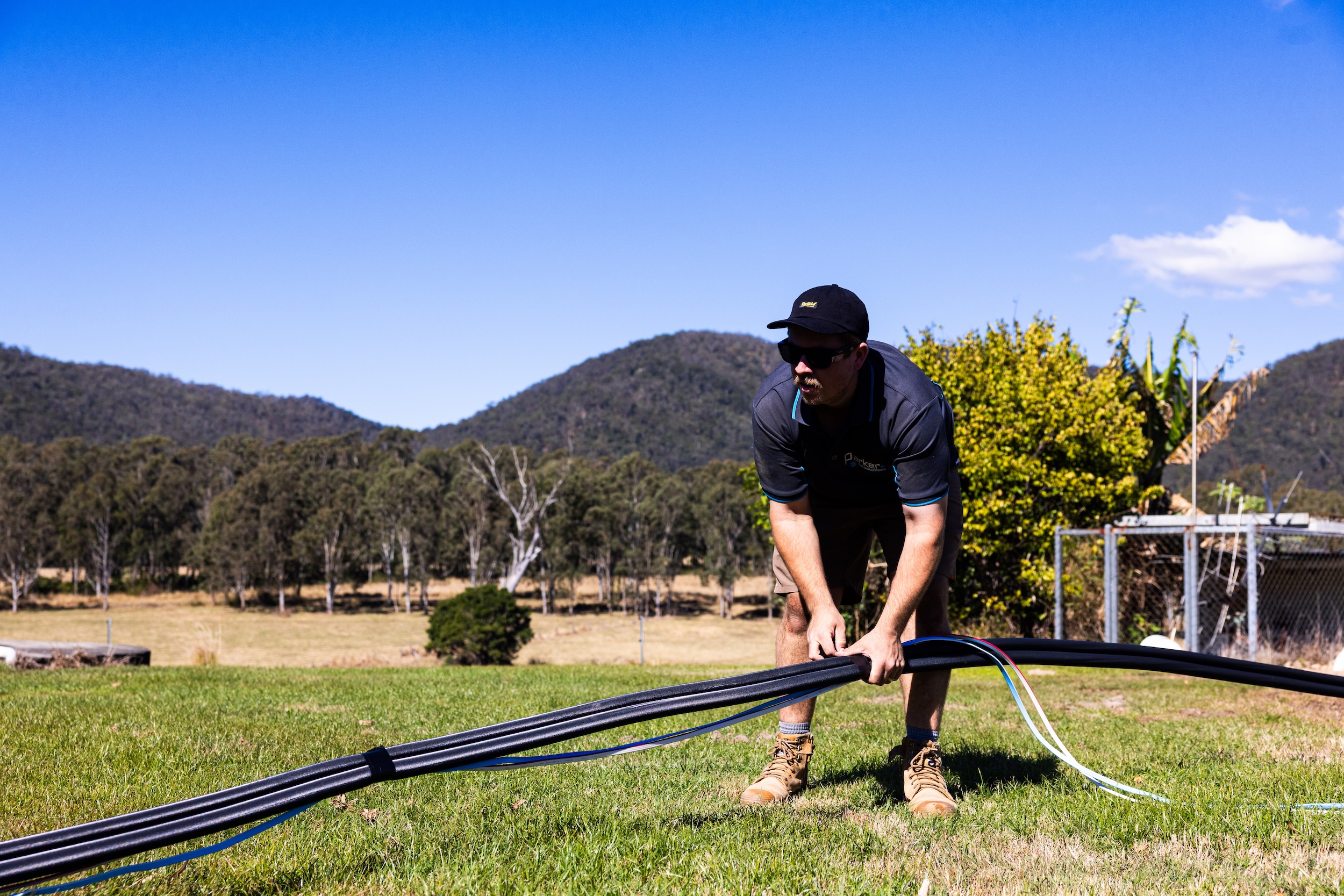 Close-up of a technician in a black Parker Air polo shirt preparing black insulated refrigeration piping on a lawn.