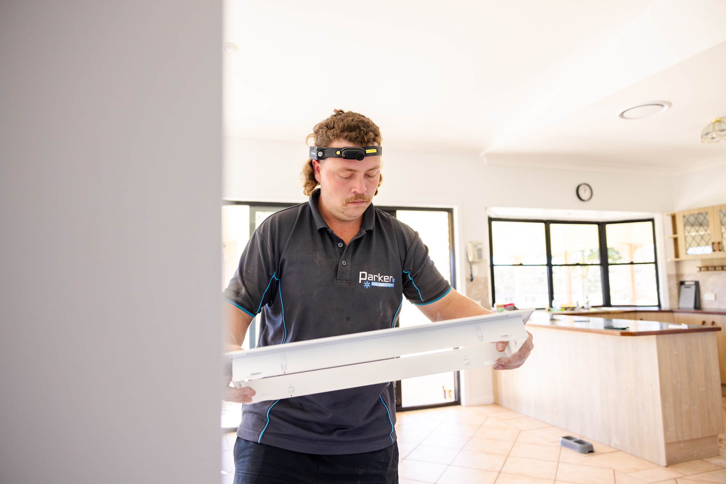 Parker Air Solutions team member carrying a white linear slot diffuser fascia in a modern home interior.