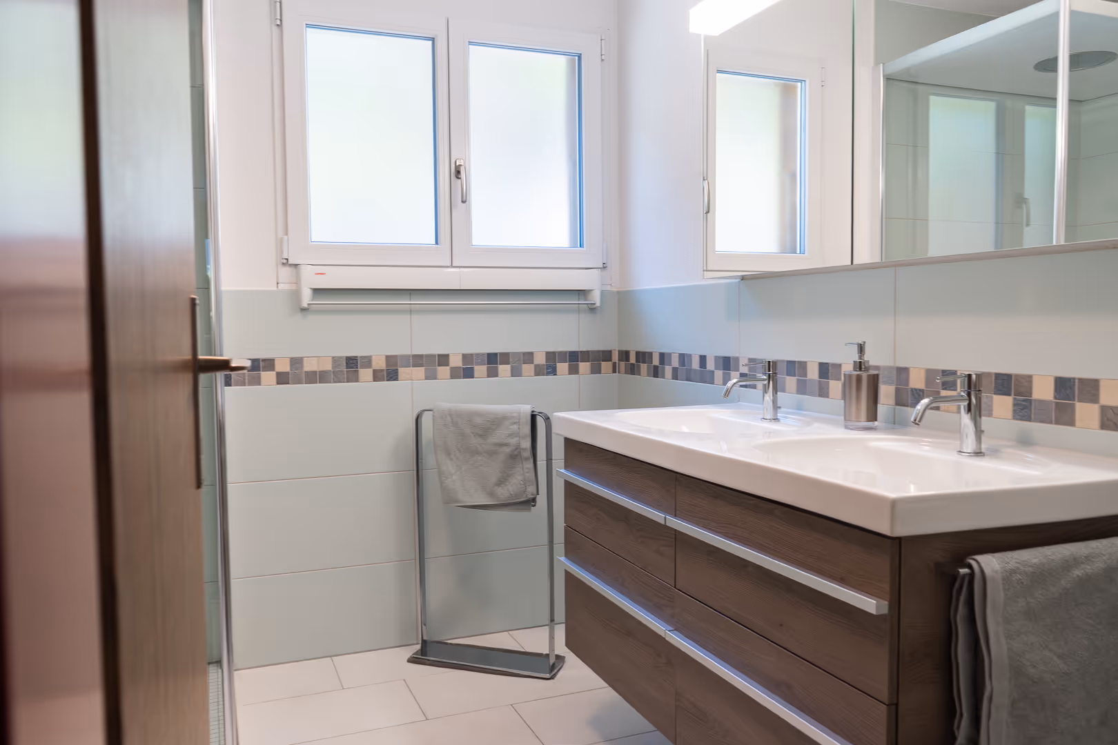 Modernes Badezimmer in einer Ferienwohnung in Adelboden mit Doppelwaschbecken und grossen Fenstern.