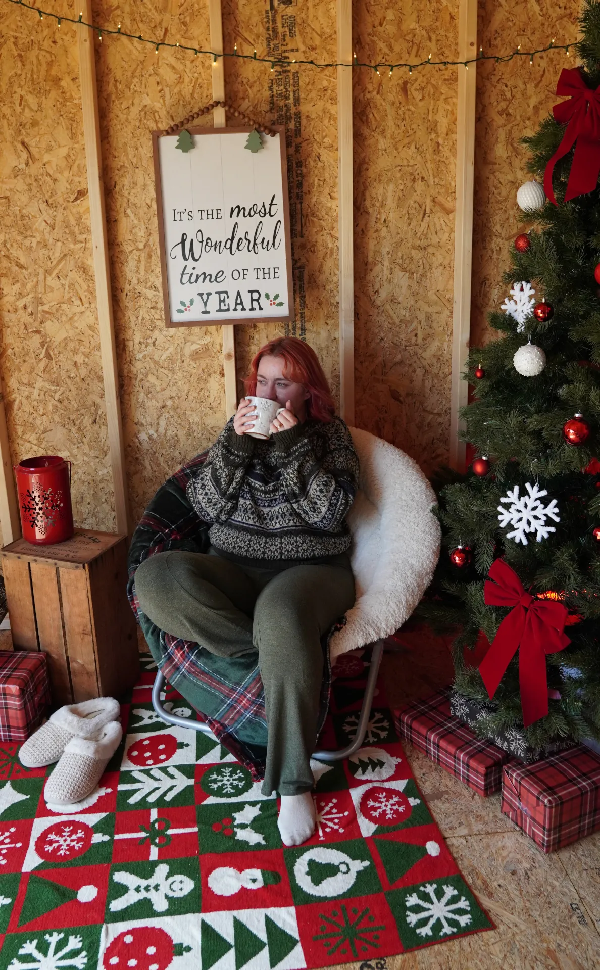 woman sitting next to a christmas tree in a cozy chair drinking coffee