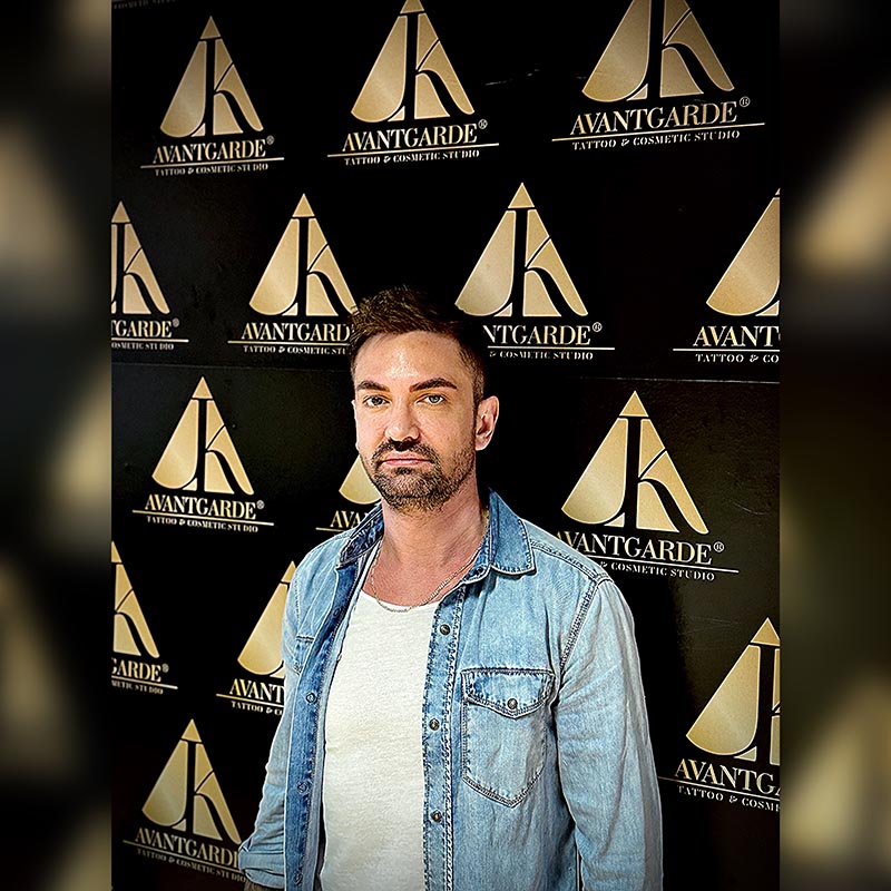 Person mit Jeanshemd vor einer schwarz-goldenen Logowand.