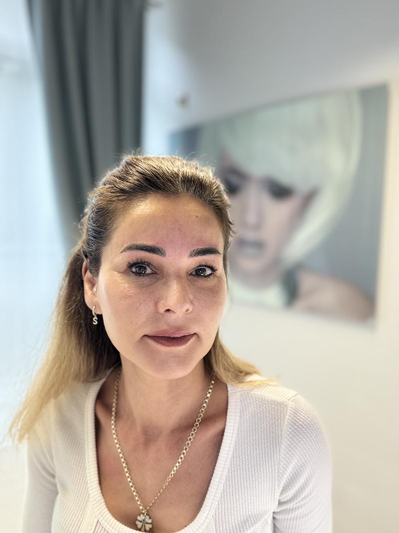 Porträt mit zurückgebundenem blondem Haar und weißem Oberteil.
