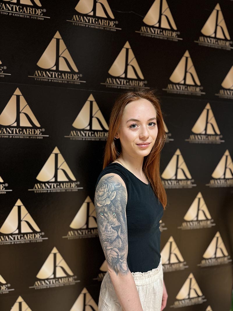 Person mit großflächigem Armtattoo vor einer schwarz-goldenen Logowand.