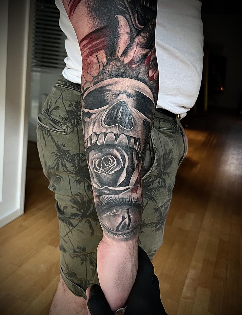 Schwarzgraues Tattoo mit Totenkopf und Rose am Unterarm.