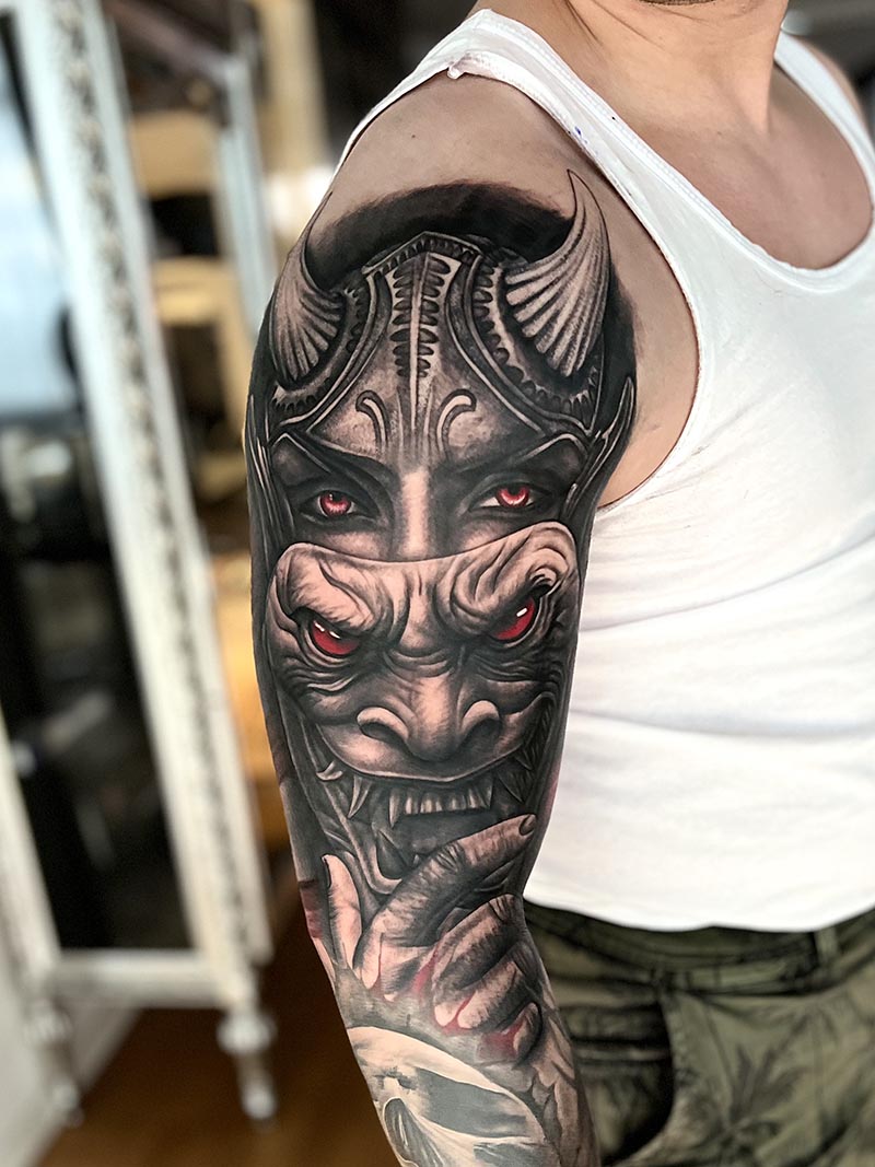 Schwarz-rotes Maskenmotiv mit Hörnern am Oberarm.