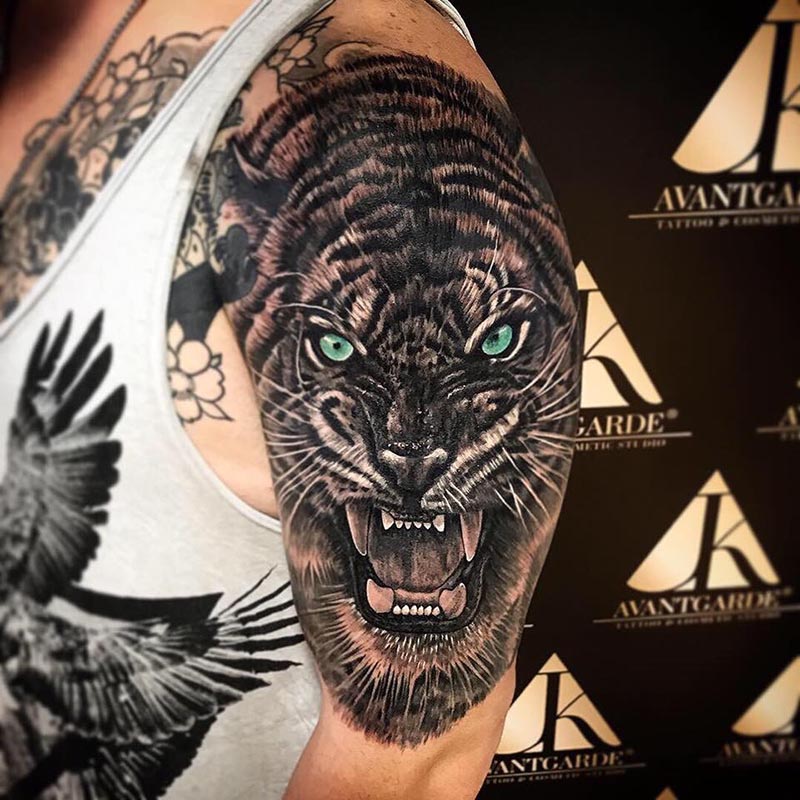 Tattoo eines Tigerkopfs mit geöffnetem Maul und hellen Augen.