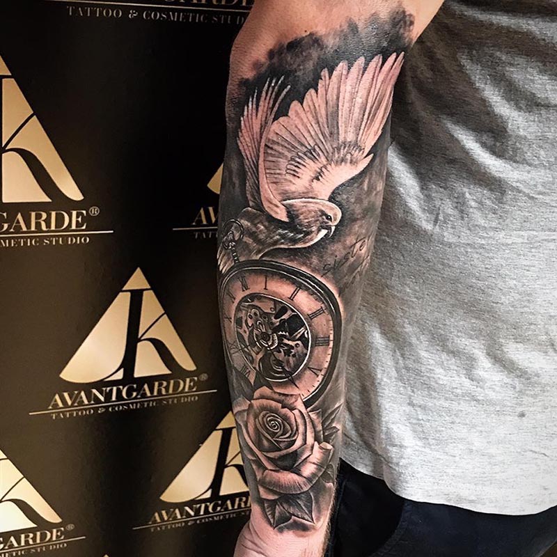 Schwarzgraues Tattoo mit ausgebreiteten Vogelflügeln und runden Ornamenten am Arm.