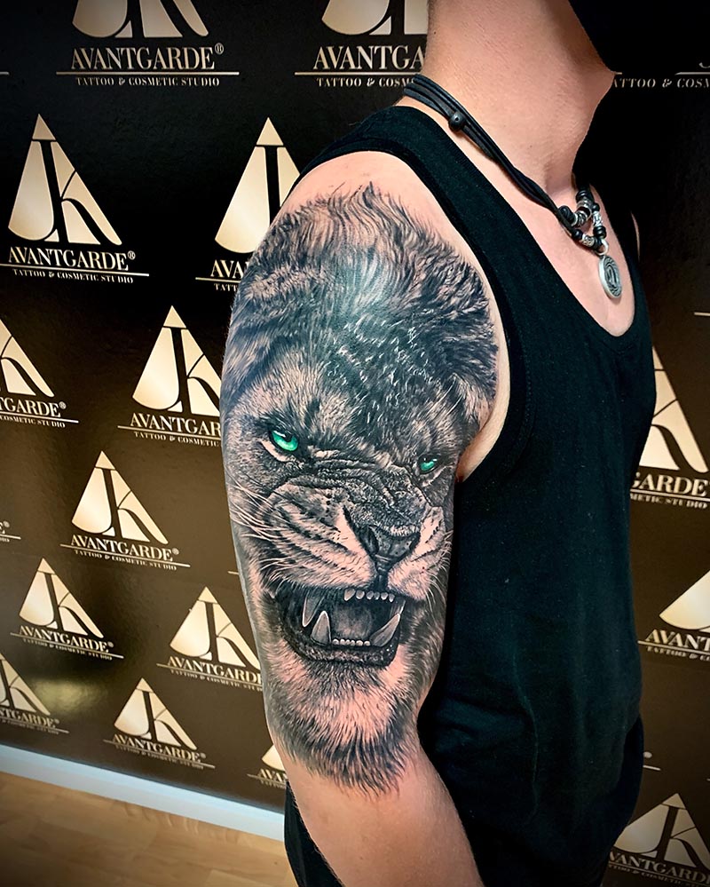Schwarzgraues Oberarmtattoo mit einem Tierkopf und einer Waldlandschaft.