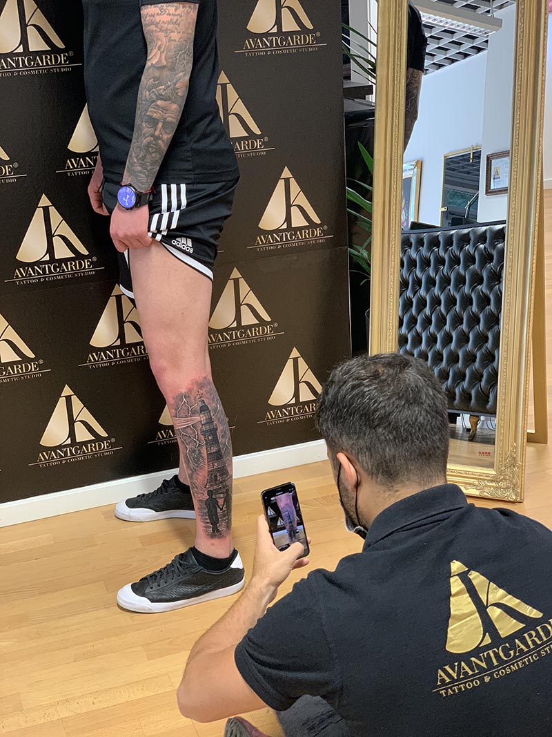 Studioaufnahme einer Person, die ein Tattoo am Unterschenkel mit einem Smartphone fotografiert.