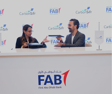 Two professionals exchanging documents across a table with First Abu Dhabi Bank and CarbonSifr logos in the background.