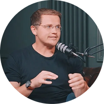Man wearing glasses and a black shirt speaking into a microphone in a podcast studio.