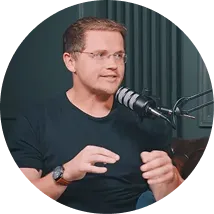 Man wearing glasses and a black shirt speaking into a microphone in a podcast studio.