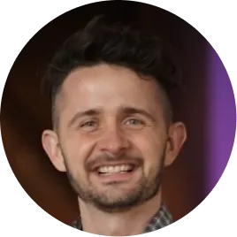 Smiling man with short curly hair and a trimmed beard in a circular frame.