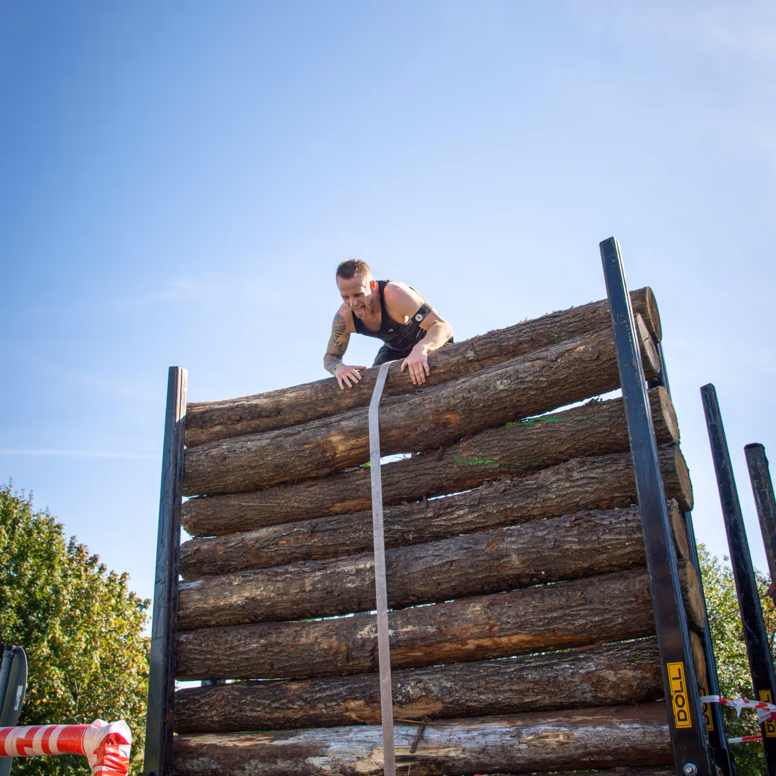 Hindernis des Elements "Luft". Ein Teilnehmer klettert über einen Lkw, beladen mit Holzstämmen.
