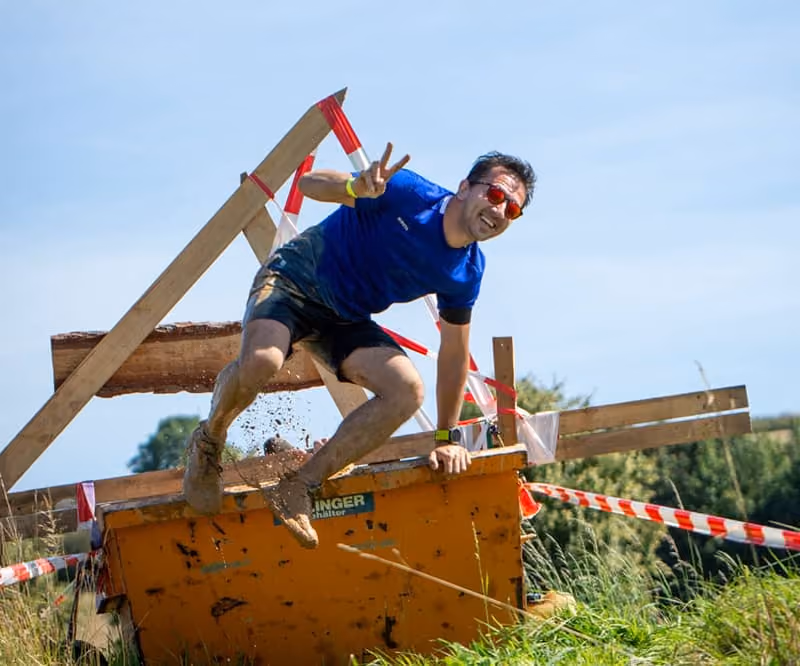 Ein Erz-X-Cross Sportler klettert aus einem mit Schlamm & Matsch befüllten Baucontainer